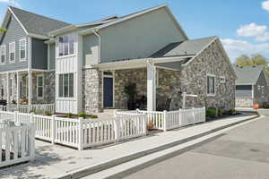 View of front of home featuring board and batten siding, stone siding, a shingled roof, stucco siding, and a fenced front yard