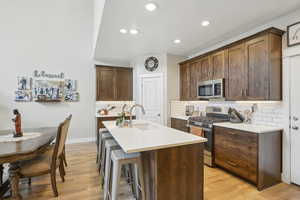 Kitchen featuring a kitchen island with sink, decorative backsplash, stainless steel appliances, light wood-style floors, and a sink