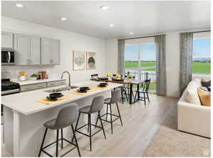 Kitchen with appliances with stainless steel finishes, a sink, light wood finished floors, a kitchen island with sink, and a kitchen breakfast bar