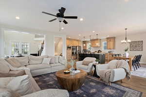 Living area featuring recessed lighting, wood finished floors, stairs, and ceiling fan with notable chandelier