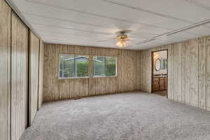 Spare room with carpet flooring, a sink, visible vents, wood walls, and ceiling fan
