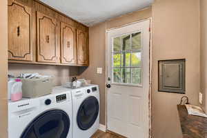 Laundry room with a textured ceiling, electric panel, washer and dryer, cabinet space, and wood finished floors