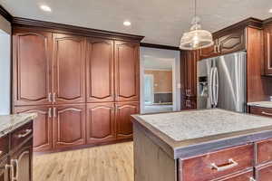 Kitchen featuring light stone counters, a kitchen island, light wood-style flooring, stainless steel fridge, and hanging light fixtures