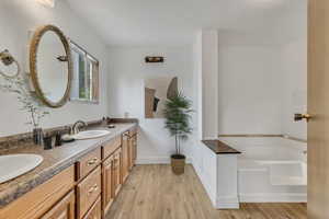 Bathroom featuring double vanity, wood finished floors, a garden tub, and a sink