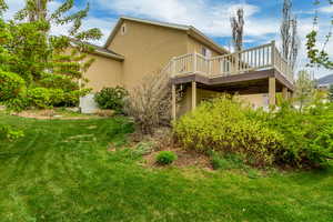 Rear view of house featuring a wooden deck, a lawn, and stucco siding