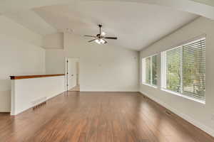 Spare room featuring dark wood-style floors, vaulted ceiling, baseboards, visible vents, and ceiling fan