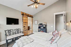 Primary bedroom featuring carpet flooring, a barn door, baseboards, a ceiling fan, and high vaulted ceiling