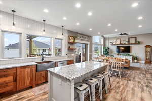 Kitchen with brown cabinets, recessed lighting, light stone counters, a copper farmhouse sink, and light wood-style floors