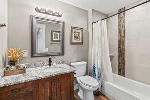 Bathroom featuring wood finished floors, toilet, vanity, and shower / bathtub combination with curtain