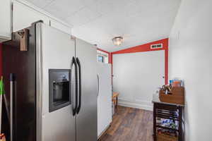 Kitchen featuring dark wood-style flooring, vaulted ceiling, freestanding refrigerator, visible vents, and stainless steel refrigerator with ice dispenser