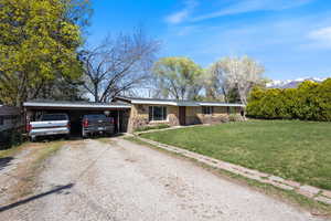 Ranch-style home featuring dirt driveway, stone siding, a front yard, and an attached carport
