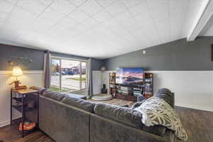 Living room featuring vaulted ceiling, a wainscoted wall, and wood finished floors