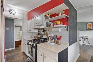 Kitchen featuring dark wood-type flooring, stainless steel range with gas cooktop, open shelves, and under cabinet range hood