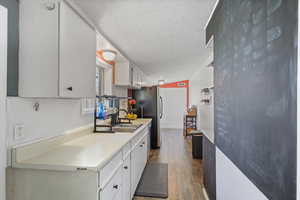 Kitchen with a sink, dark wood finished floors, freestanding refrigerator, white cabinetry, and light countertops