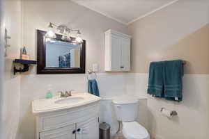 Bathroom featuring toilet, vanity, tile walls, crown molding, and wainscoting
