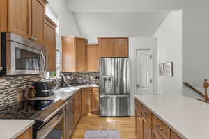 Kitchen featuring a sink, wood cabinetry, decorative backsplash, light wood-style floors, and stainless steel appliances