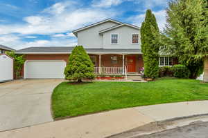 Traditional-style home featuring a front lawn, covered porch, concrete driveway, brick siding, and an attached garage