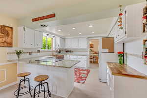 Kitchen featuring a peninsula, electric cooktop, white cabinetry, decorative backsplash, and light stone counters