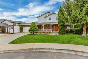 Traditional home with driveway, covered porch, an attached garage, a shed, and a front yard