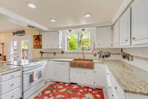 Kitchen featuring a peninsula, a sink, white appliances, and a wealth of natural light