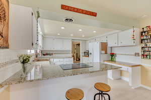 Kitchen featuring a peninsula, stainless steel microwave, backsplash, white refrigerator with ice dispenser, and cooktop