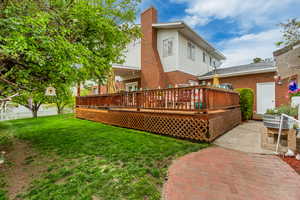 Rear view of property with brick siding, a yard, a wooden deck, and a chimney