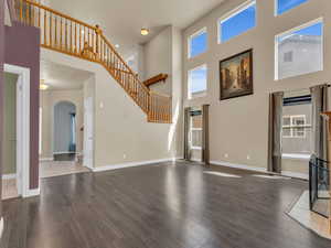 Unfurnished living room with wood finished floors, a towering ceiling, arched walkways, and a healthy amount of sunlight