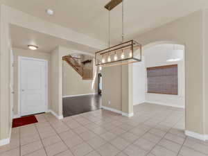 Unfurnished dining area with arched walkways, stairway, baseboards, and light tile patterned floors