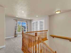 Hallway with an upstairs landing, a textured ceiling, baseboards, carpet flooring, and recessed lighting