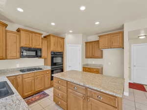 Kitchen featuring black appliances, light stone counters, a center island, and light tile patterned floors