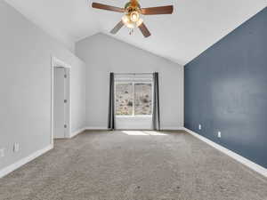 Carpeted empty room featuring ceiling fan, lofted ceiling, and baseboards