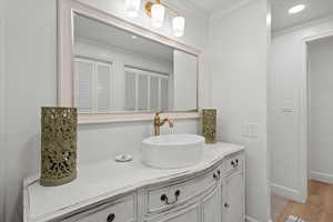 Bathroom featuring baseboards, wood finished floors, vanity, and ornamental molding