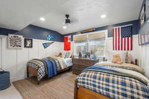 Bedroom with light colored carpet, ceiling fan, a decorative wall, and a textured ceiling