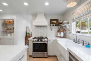Kitchen with stainless steel range with gas cooktop, custom range hood, open shelves, light countertops, and ornamental molding