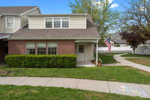 View of front of home with brick siding, a front lawn, fence, and a shingled roof
