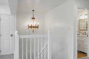 Hallway featuring an upstairs landing, crown molding, a notable chandelier, and a sink
