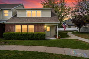 View of front of house with fence, a shingled roof, a front lawn, and brick siding