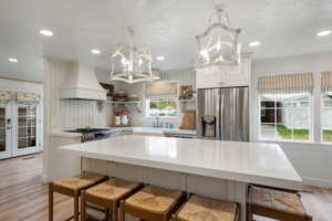 Kitchen featuring stainless steel appliances, light countertops, a sink, premium range hood, and a chandelier