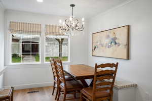 Dining room featuring baseboards, visible vents, a chandelier, wood finished floors, and crown molding