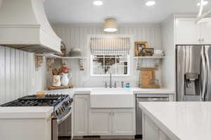 Kitchen with stainless steel appliances, a sink, open shelves, light countertops, and premium range hood