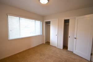Unfurnished bedroom featuring baseboards, two closets, and light carpet