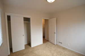 Unfurnished bedroom featuring light carpet, visible vents, a closet, and baseboards