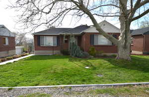 View of front facade with brick siding, a front yard, and roof with shingles