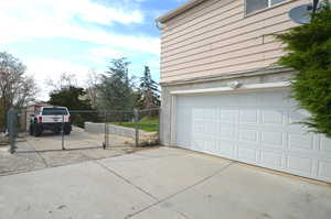 Garage with fence, a gate, and concrete driveway to backyard.