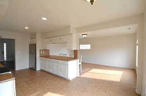 Kitchen featuring light tile patterned floors, white cabinets, freestanding refrigerator, a kitchen breakfast bar, and recessed lighting