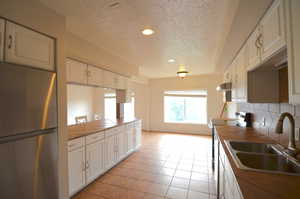 Huge - Natural Light Kitchen with freestanding refrigerator, a textured ceiling, a sink, range with electric stovetop, and tile counters