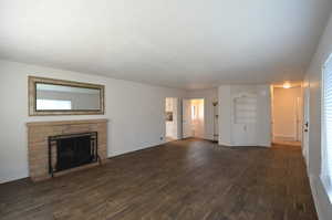Unfurnished living room with dark wood-style flooring, a stone fireplace