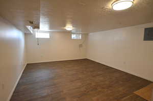 Below grade area featuring baseboards, electric panel, new dark wood-style floors, a textured ceiling, and visible vents
