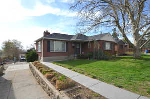 View of front of property with a chimney, driveway, a front lawn, brick siding, and a shingled roof