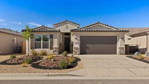 View of front of house with a tiled roof, stone siding, concrete driveway, an attached garage, and stucco siding